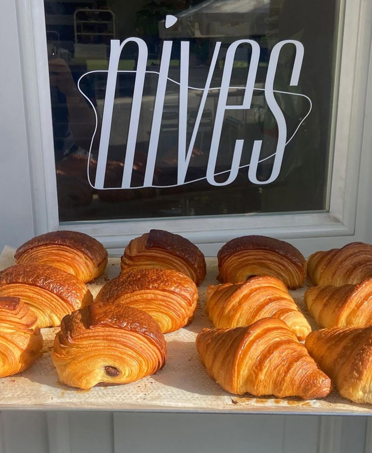 Het nives-logo op het raam met een mand verse croissants ervoor